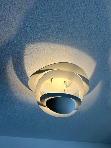 Deckenlampe mit geschwungenem Design und sanften Schatteneffekten an der Wand.