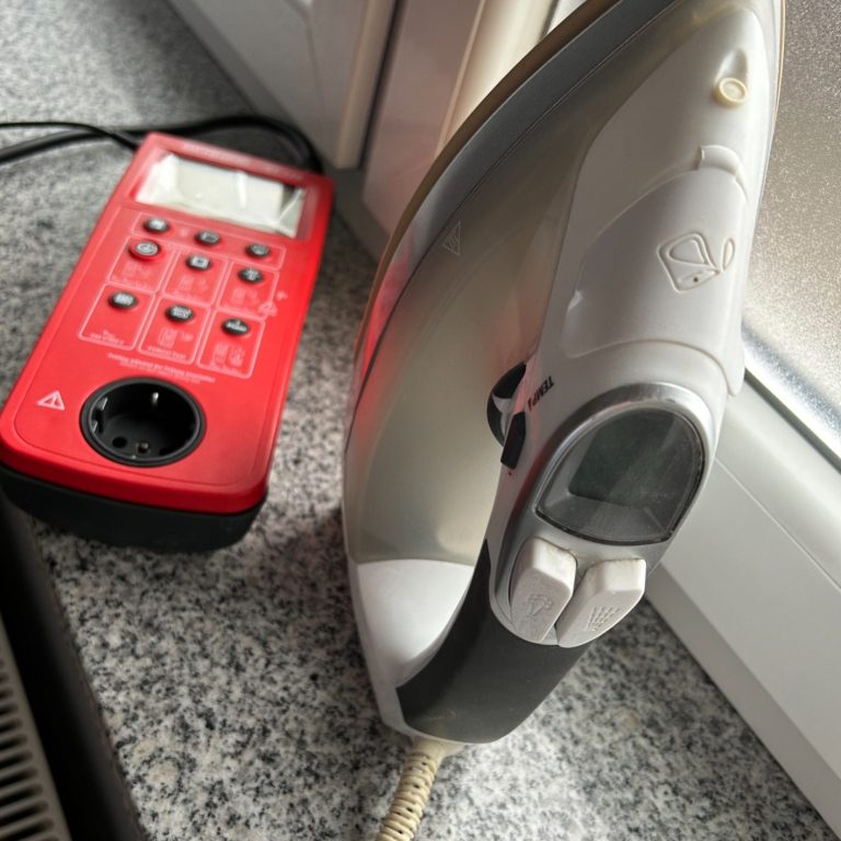 Ein Dampfbügeleisen neben einer roten Mehrfachsteckdose auf einer grauen Arbeitsplatte.