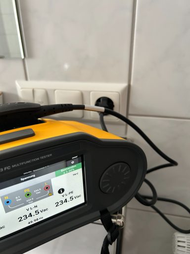 Ein gelbes Gerät mit Display und Stecker, das an eine Wandsteckdose angeschlossen ist.