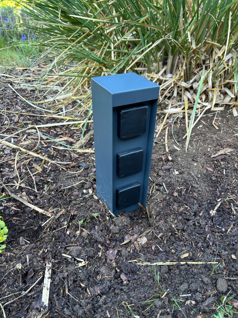 Installation einer Steckdosensäule im Garten Dunkelgrauer Stromverteiler in einem Garten zwischen Pflanzen.