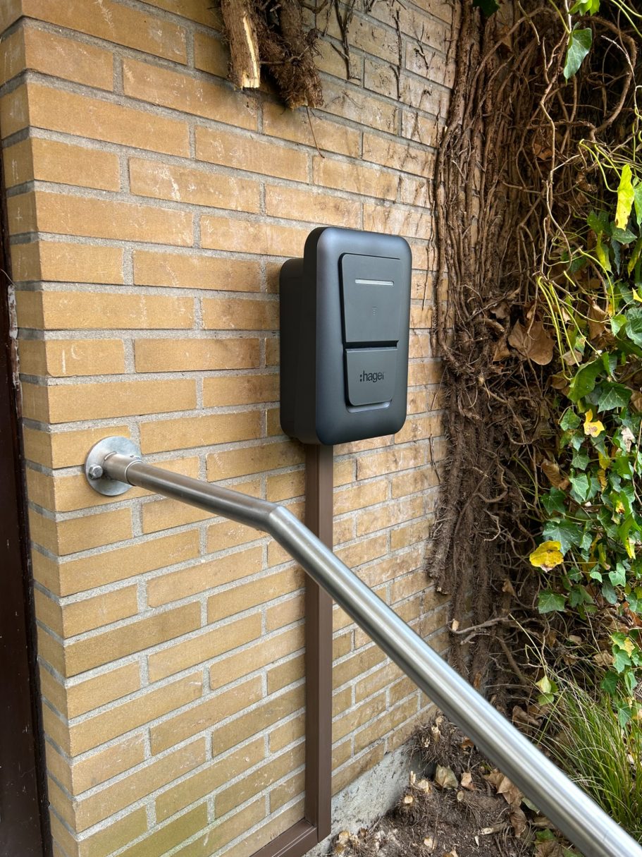 Montage und Anschluss einer Wallbox Schwarze Box an einer Ziegelwand mit einem Handlauf daneben.